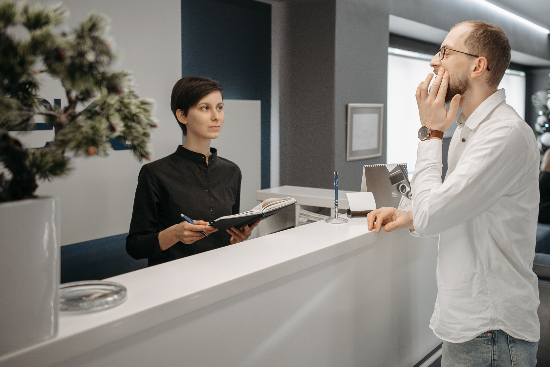 Patient am Empfang einer Praxis im Gespräch mit einer Mitarbeiterin