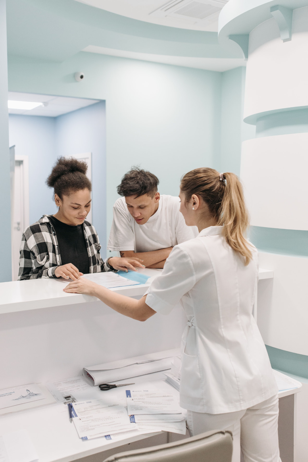 Praxisteam am Counter erklärt zwei Patient:innen ein Formular